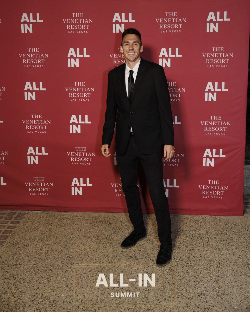 Andrew Rusk in a black suit in front of the All-In Summit and Venetian Resort backdrop
