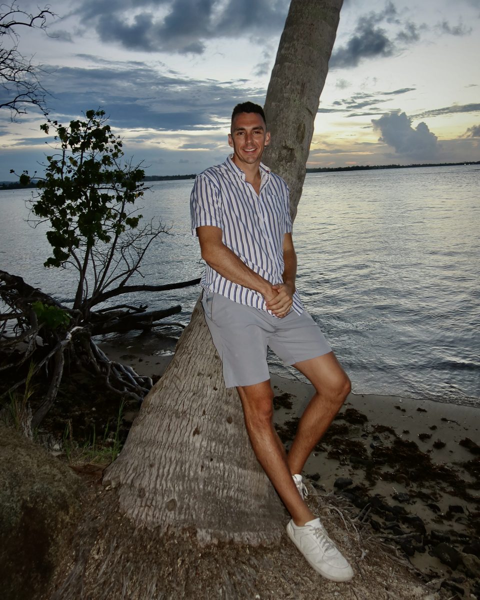 Andrew Rusk leaning on a palm tree by the water at dusk in Tampa Bay